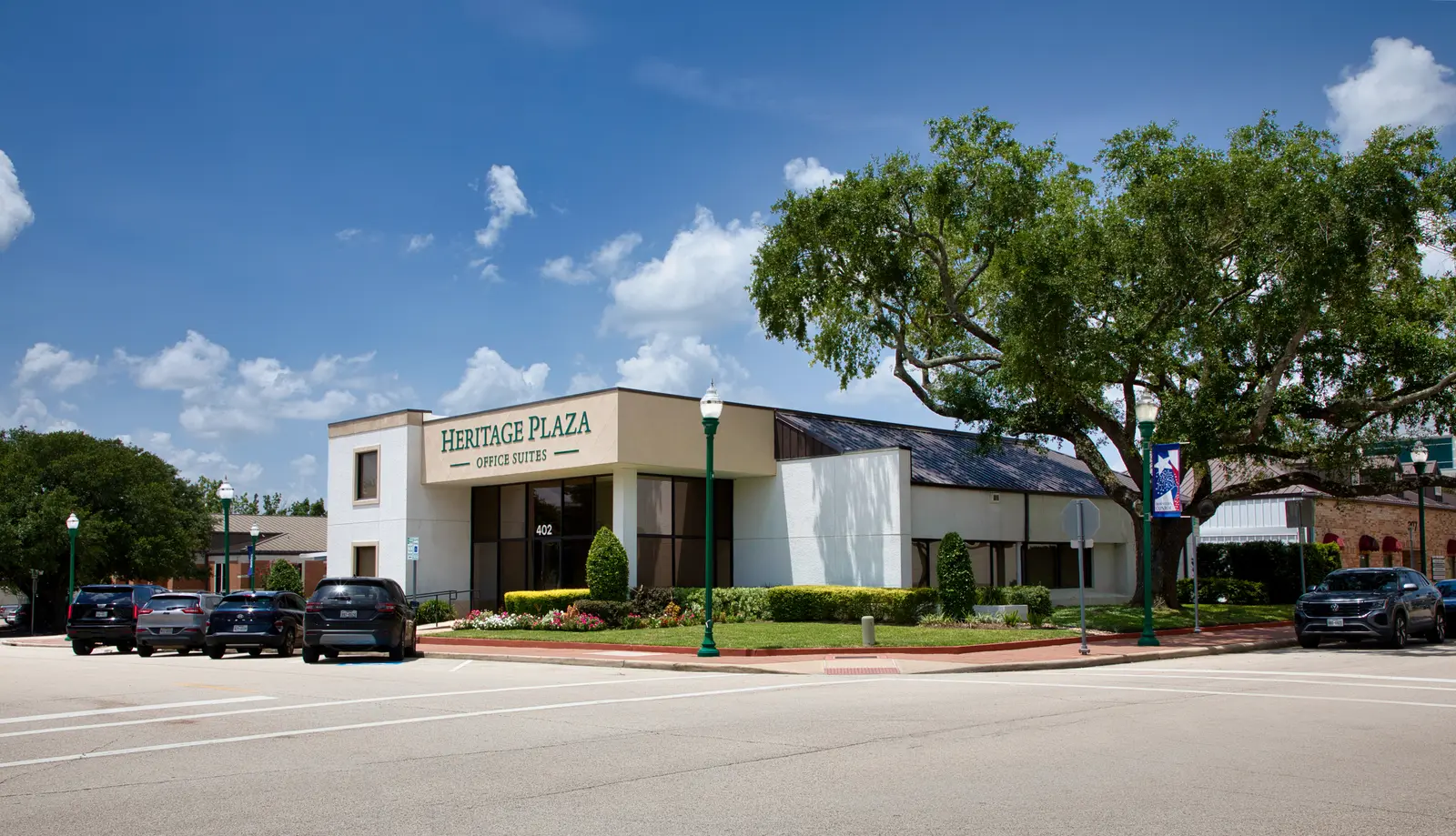 Heritage Plaza seen from across Simonton Street — the full frontage, street lamps, and a large live oak under a blue sky