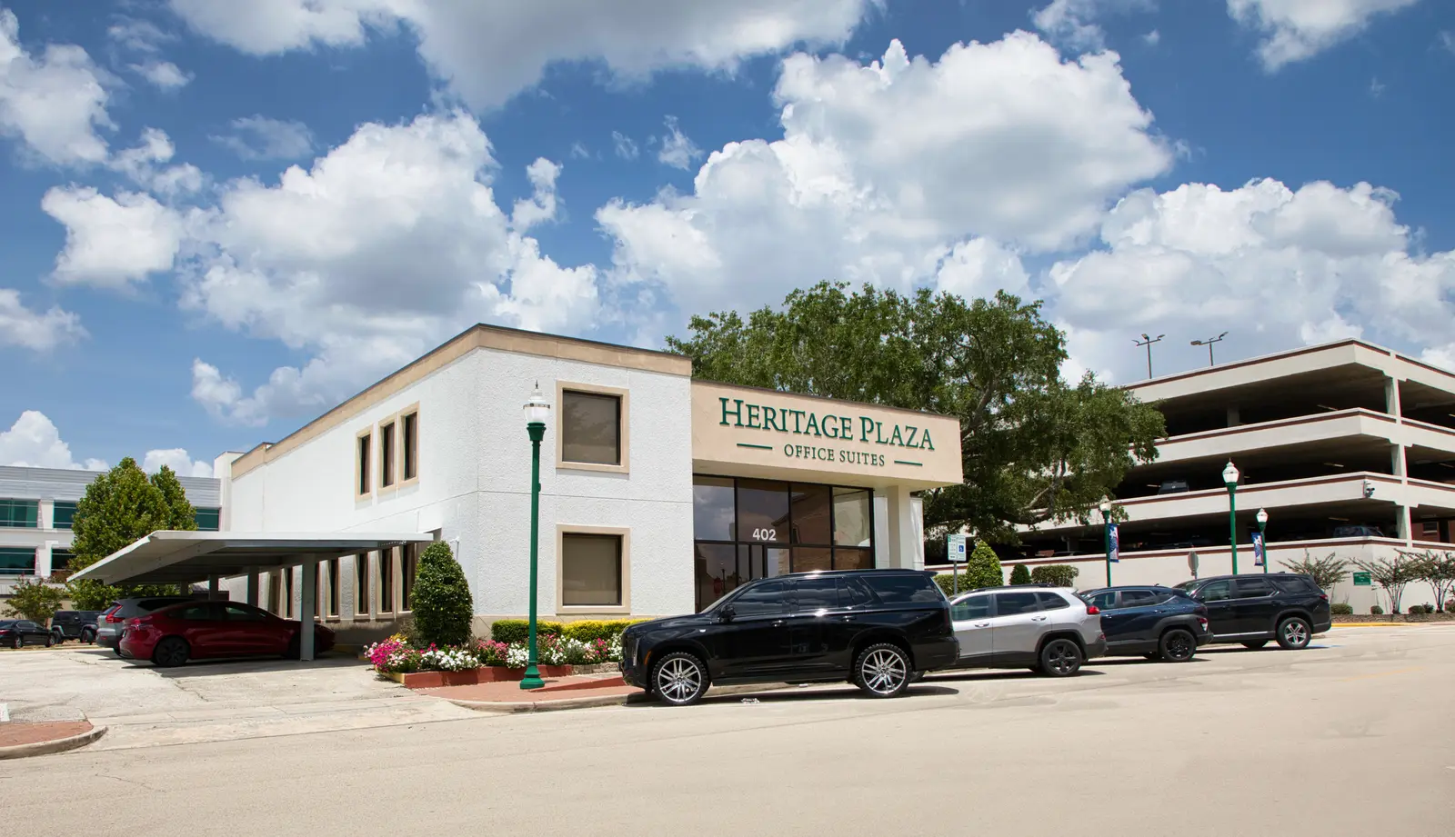 Wide view of Heritage Plaza beside the adjacent multi-level covered parking garage, with a covered carport alongside the building